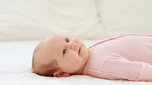close-up portrait of a small newborn baby girl with blue eyes lies on a white cotton bed at home and smiles