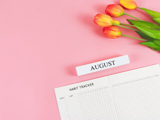 flat lay of habit tracker book with wooden calendar August,   and tulips  on pink background.