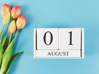  flat lay of wooden calendar with date August 01 on blue  background with orange and yellow tulips, copy space.