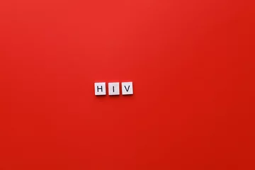 Fotobehang HIV Day. AIDS Day. Flatly inscription hiv from wooden letters on a red background © upssallaaa