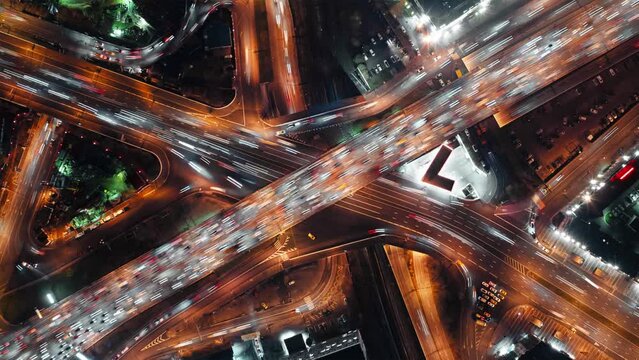 Top-down time-lapse view of fast-moving cars on a highway, intense traffic during rush hour at a city crossroad, modern multi-level intersection with beautifully moving vehicles.