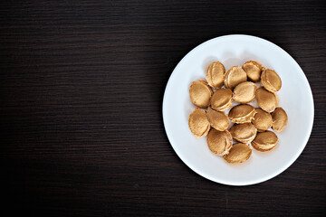 Apricot pits lie on a white plate on a dark background. View from above. Vitamin B 17. Healthy food background. There is space for text