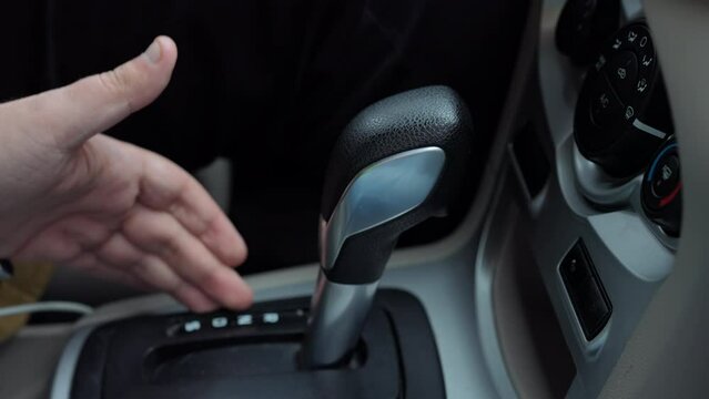 Close-up gear shift with male hand pointing and female palm holding equipment. Close-up part of car with unrecognizable Caucasian man teaching woman driving automobile