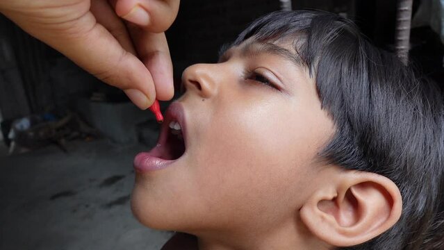 An Asian boy is being fed a vitamin A capsule by mouth. 