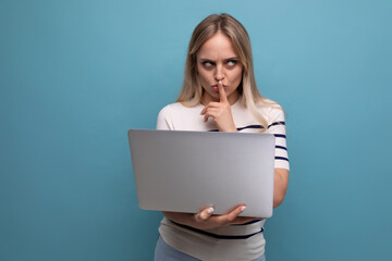 pensive young woman student with a laptop in her hands laughing while chatting on the phone looks away on a blue isolated background with copy space