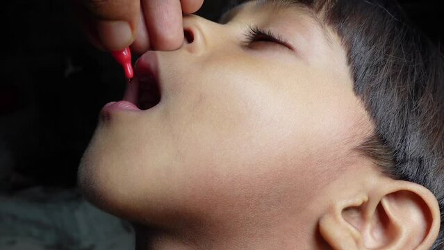 An Asian boy is being fed a vitamin A capsule by mouth. 