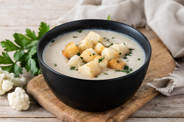 Cauliflower soup in a black bowl on wooden table