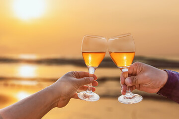 friends hands raise a toast with glasses of red colored wine on sea sunset background
