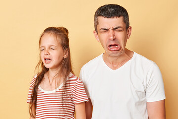 Fototapeta premium Funny father and daughter wearing casual t-shirts standing isolated over beige background crying grimacing expressing sadness and sorrow hearing bad news.