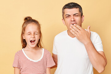 Sleepy tired exhausted father and daughter wearing casual t-shirts standing isolated over beige background looks sleepless yawning covering mouth with hands.