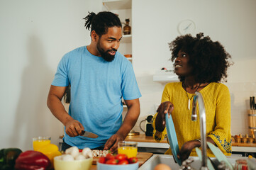 Fototapeta na wymiar A happy multiracial couple in the kitchen at home preparing a meal and washing dishes.