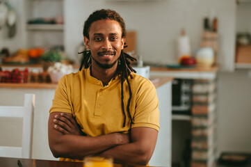Portrait of a handsome multicultural man sitting at home with arms crossed and smiling at the...