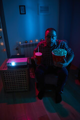 Fototapeta na wymiar Man enjoying popcorn and juice while watching movie at home projector.