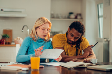 A pensive multiracial couple is looking at bills and doing calculations at home.