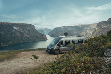 Camper Van parkt auf felsigem Grund vor Bergen und einem Fjord