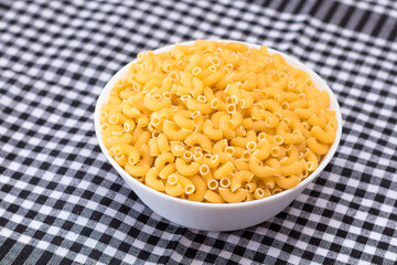 Uncooked Chifferi Rigati Pasta in White Cup on Black Checkered Towel. Fat and Unhealthy Food. Classic Dry Macaroni. Italian Culture and Cuisine. Raw Pasta