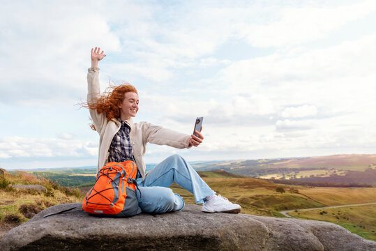 Happy woman in jacket and backpack reaching the destination, on the top of mountain  and taking photos by phone at sunset. Travel  Lifestyle concept The national park Peak District in England