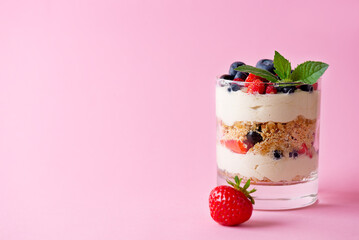 Trifle dessert in a glass with berries, mint, whipped cream and biscuit on a pink background. Healthy food, vegan, sugar, gluten and lactose free.