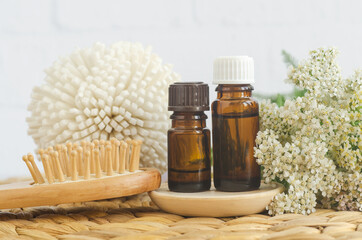 Small bottles with essential yarrow oil, wooden hairbrush and yarrow flowers. Aromatherapy, homemade beauty treatment and herbal medicine ingredients.