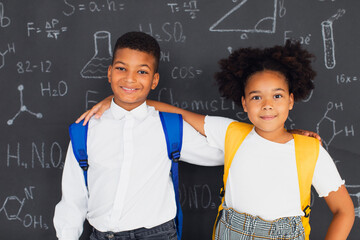 Happy African American schoolgirl and schoolboy solving problems near school board, back to school concept