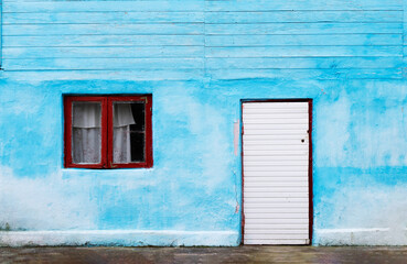 Obraz na płótnie Canvas Facade of a bright blue wall with a red framed window and a white wooden closed door of an old Georgian house