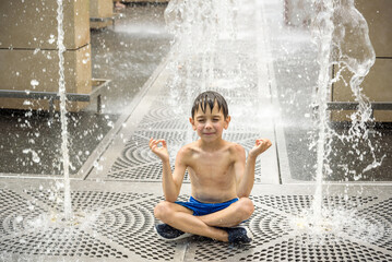 Boy meditating in water fountain find ZEN. Child playing with a city fountain on hot summer day. Happy kids having fun in fountain. Summer weather. Active leisure, lifestyle and vacation