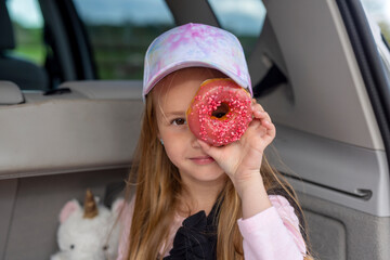 A girl covers her face with a donut in the trunk of a car