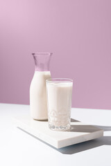 Leche fresca fría en una botella y un vaso sobre fondo rosa