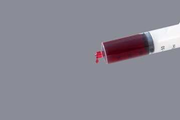 Jeringuilla vertiendo sangre sobre fondo gris