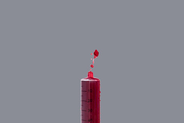 Jeringuilla vertiendo sangre sobre fondo gris