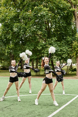 Vertical image of beautiful girls from cheerleading team dancing with pompom outdoors