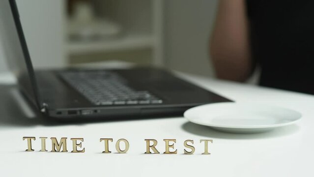 Time to rest. A woman is sitting at her workplace in front of a laptop and drinking coffee. The inscription is time to rest. The concept of a break from work.