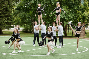 Cheerleader team doing tricks and dancing with pompom at sport competition outdoors