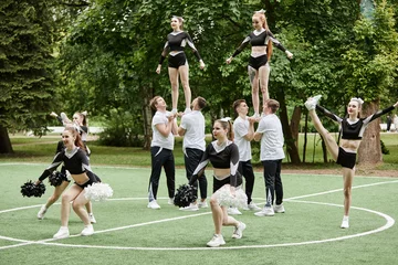 Fototapete Tanzschule Cheerleader team doing tricks and dancing with pompom at sport competition outdoors