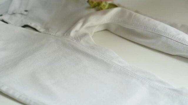 Shortening jeans. White jeans, Measuring tape, scissors on table. Jeans cutting. Hands cut off the legs of jeans with scissors