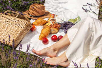 A summer picnic in a lavender field with croissants, peaches, salami, cheese and a bottle of wine and glasses.