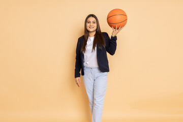 Beautiful young indian woman wearing formal suit holding basket ball in hand standing isolated over beige background.