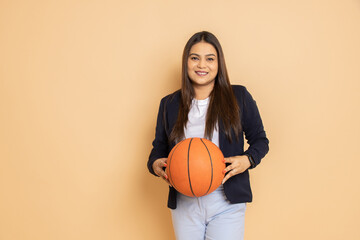 Portrait of beautiful young indian woman wearing formal suit holding basket ball in hand standing...