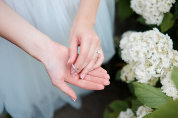 Obraz na płótnie Canvas Wedding ring concept. Beautiful bride hands playing with gorgeous ring near white blossom flowers.