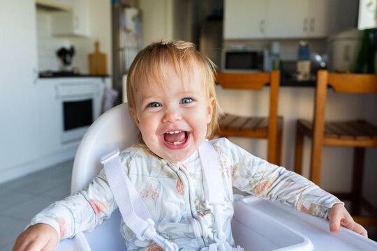 happy one year old baby girl clicked in to high chair ready for food in the morning