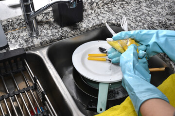 woman wearing gloves washing cutlery; dishes and pots with water and degreaser in the kitchen
