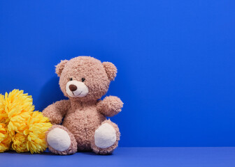 Toy bear and beautiful bright yellow flowers on a blue background. Copy space for text. Toys for kids.