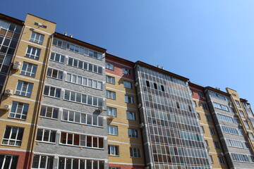 Fototapeta premium A high-rise multi-storey brick house stands against a blue sky, photo from bottom to top. 