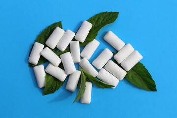 Several white pads of chewing gum with mint leaves lie on a blue background.