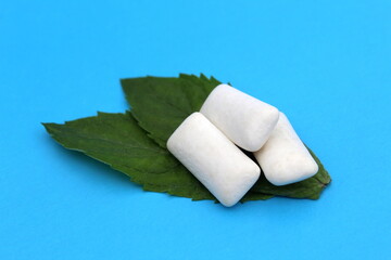 Several white pads of chewing gum with mint leaves lie on a blue background.	