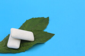 Several white pads of chewing gum with mint leaves lie on a blue background.