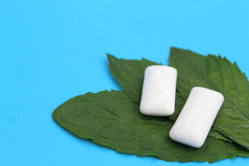 Several white pads of chewing gum with mint leaves lie on a blue background.