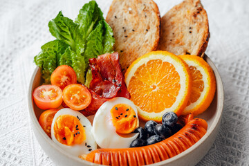 Breakfast bread, bacon, boiled eggs and fruits and vegetables.