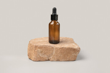 Dark amber glass bottle standing on stone. Natural skin care SPA beauty product design. Mineral organic oil cosmetics. Gray background. MockUp. Oily pipette. Face and body treatment. Front view stand