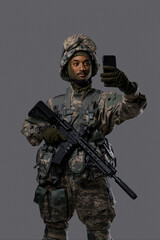 Young military man in uniform and helmet captures a selfie or video call with a smartphone, displaying the technology skills and adaptability of soldiers in uniform